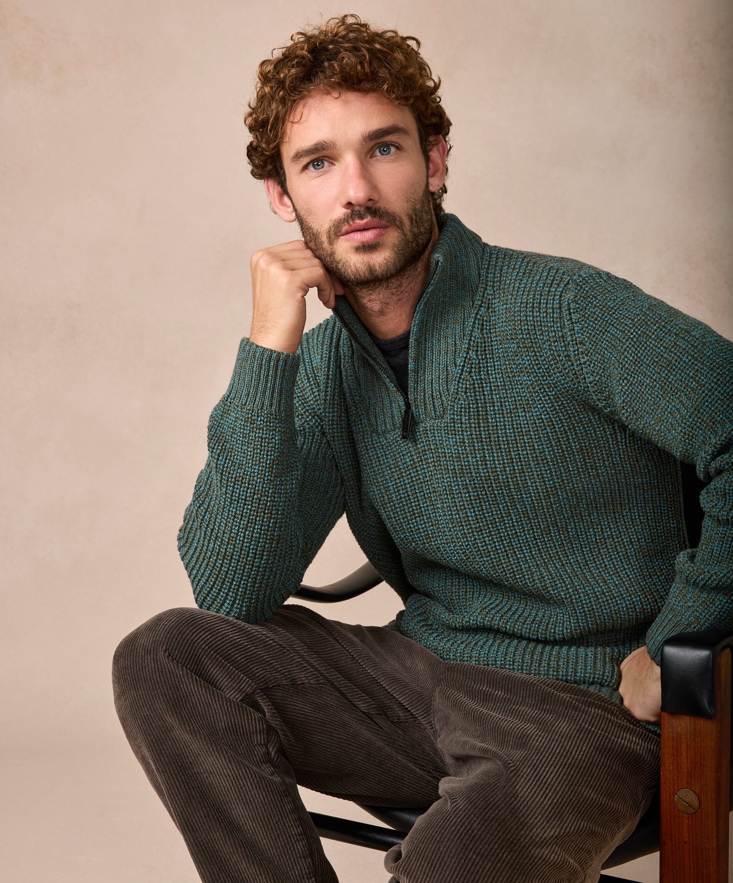 Man wearing a green knitted sweater sitting on a chair against a beige background