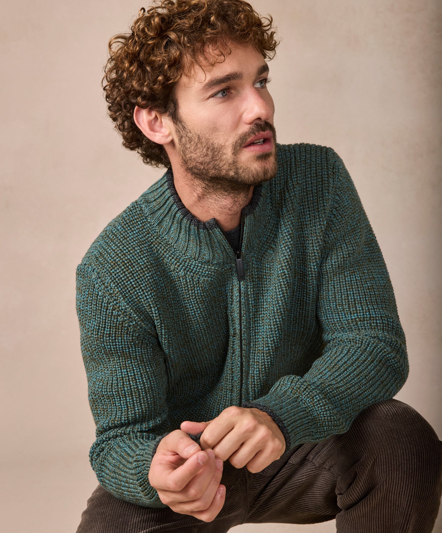 Man wearing a green knitted sweater sitting against a beige background