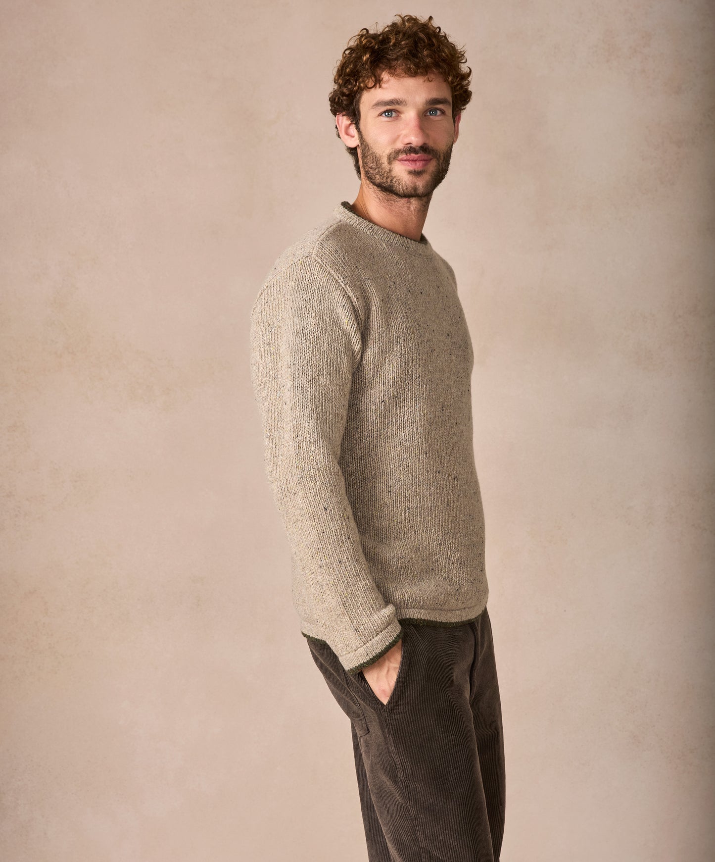 Man wearing a beige sweater and dark pants against a beige background
