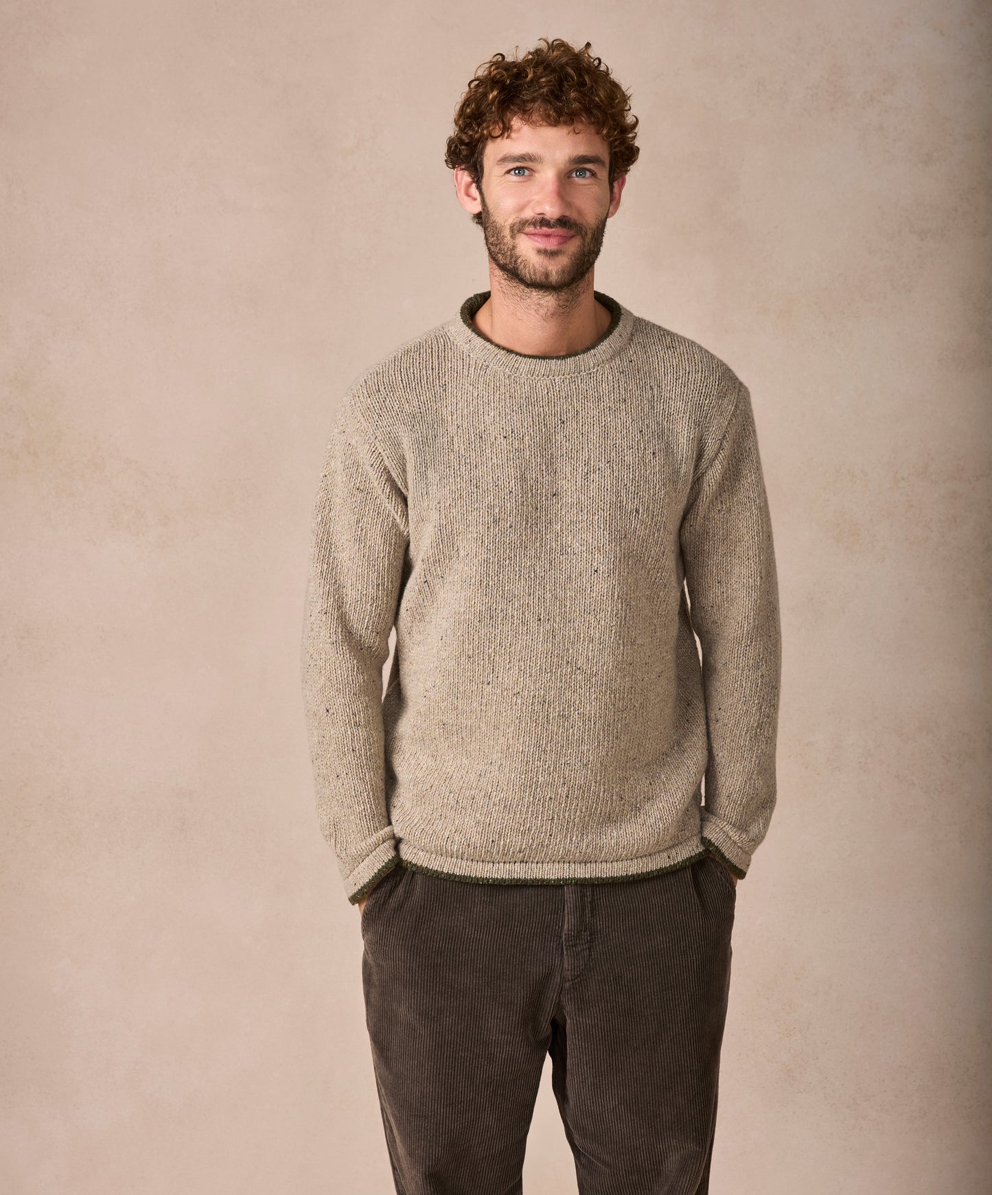 Man wearing a beige sweater and dark pants against a beige background