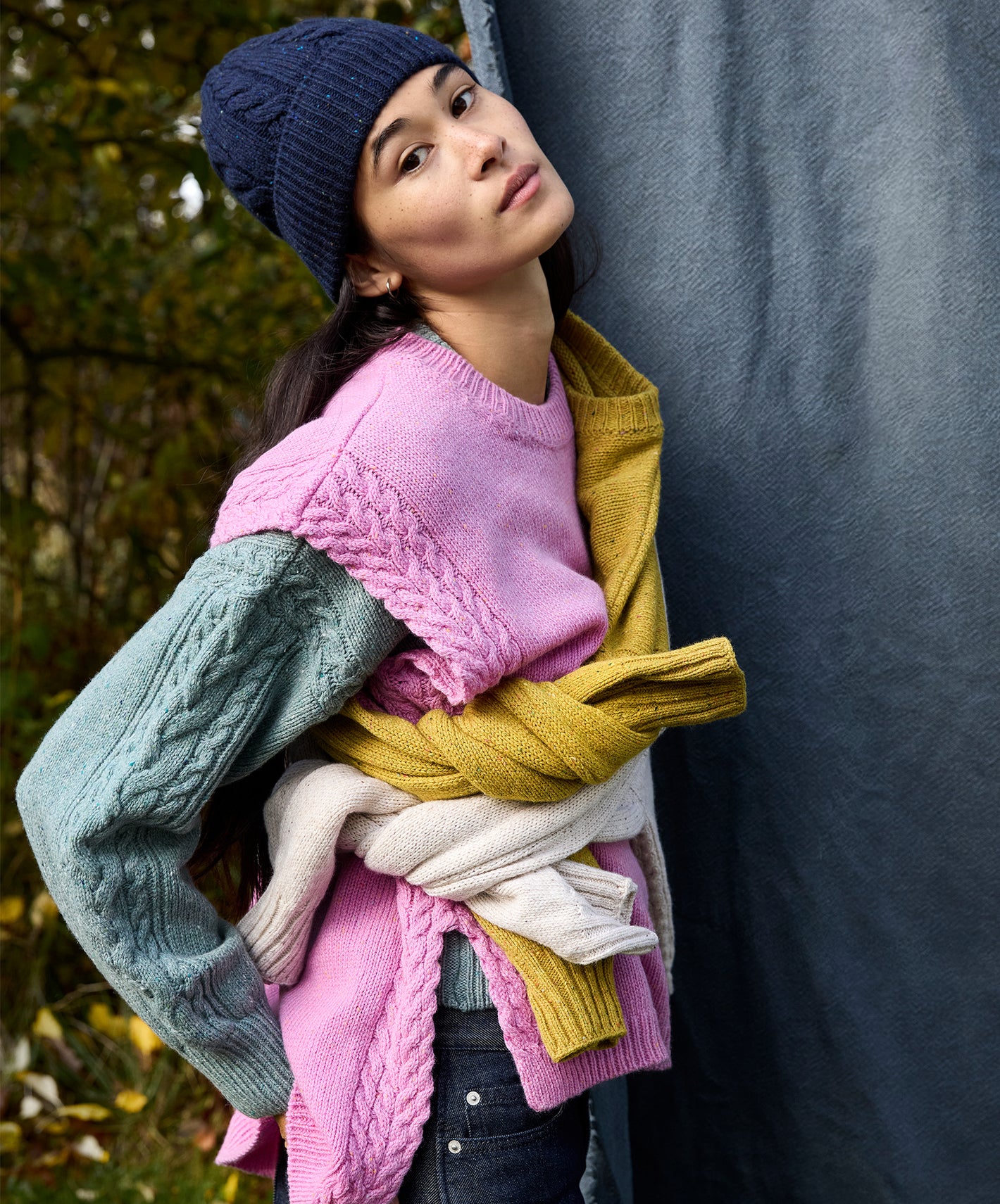 Woman holding a pile of colorful sweaters against a dark background